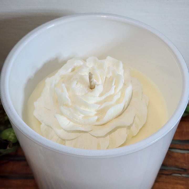 A white soy candle is shown in an opaque container. The candle wax is white with a flower detail in the wax.